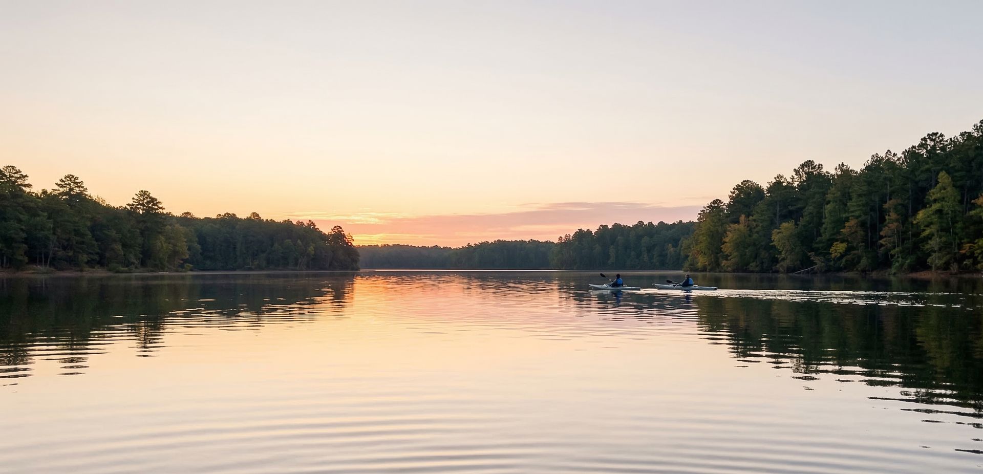 Kayakers on a calm Southern lake lined with pine trees at dusk