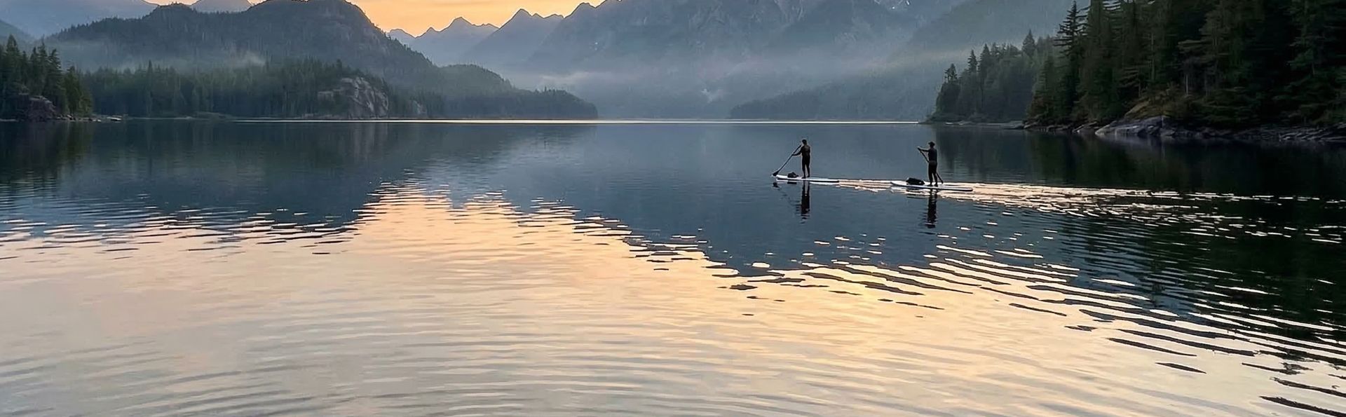 Two paddleboarders on a serene mountain lake at sunset