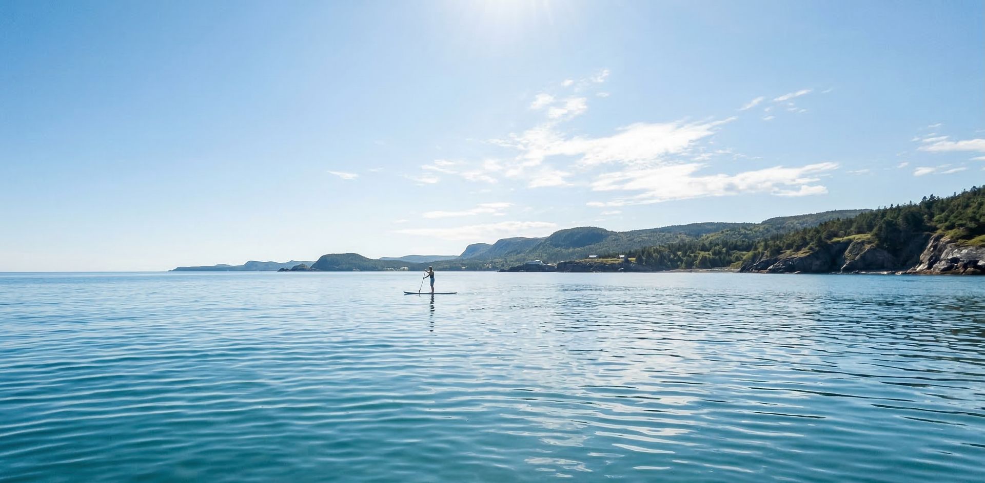 Paddleboarder on clear blue ocean water with coastal hills